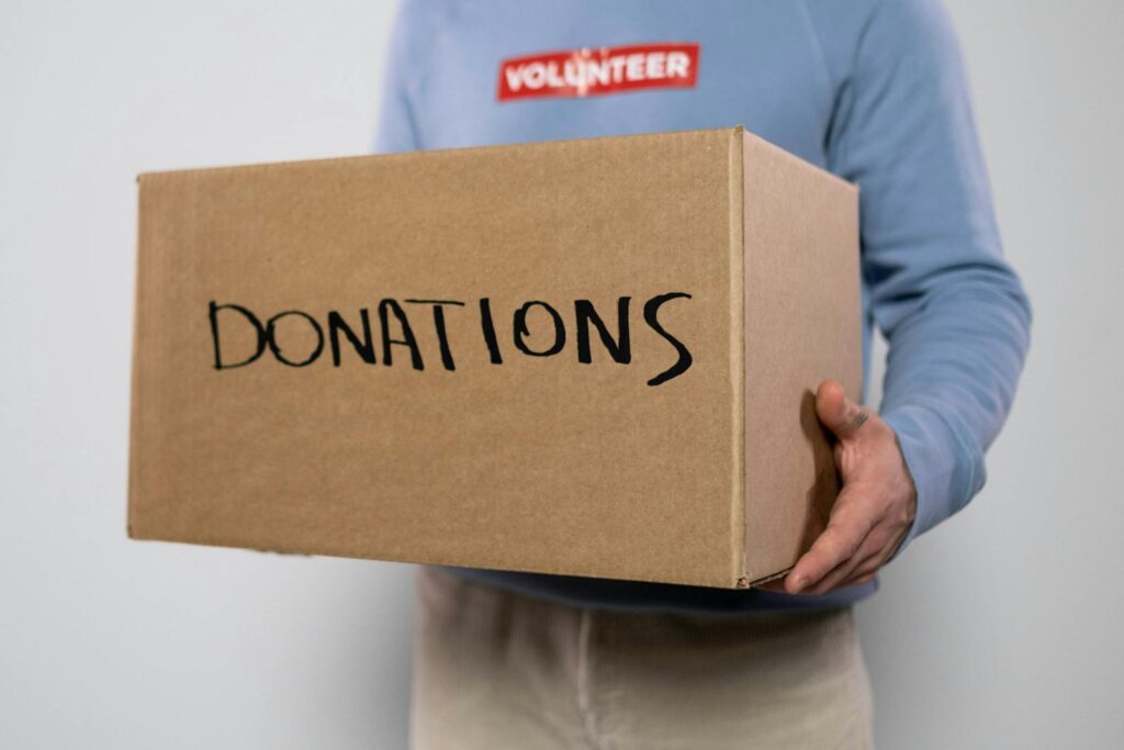 Close-up of a volunteer in a blue sweater holding a donation box. Concept of charity and volunteerism.