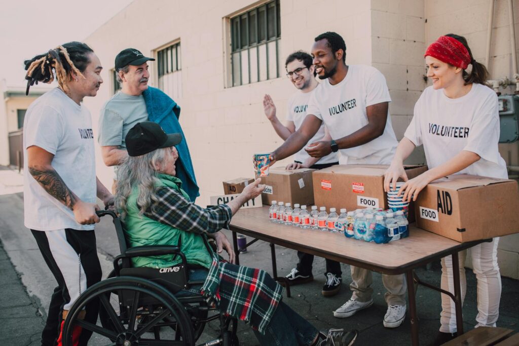 Volunteers distribute bottled water and supplies to diverse individuals in an outdoor setting, showcasing community support.