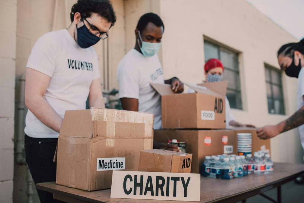 Group of volunteers wearing masks organizing donation boxes labeled food and medicine outdoors.