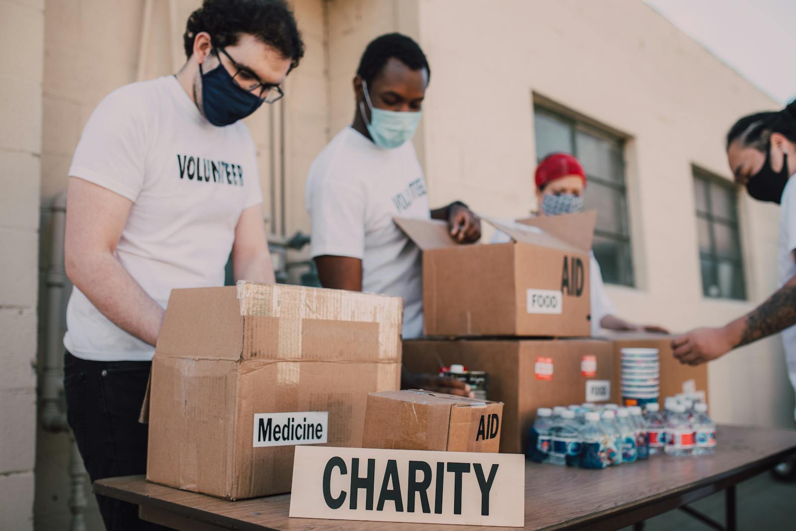 Group of volunteers wearing masks organizing donation boxes labeled food and medicine outdoors.